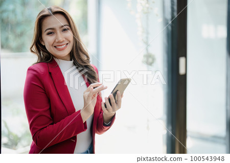Portrait of beautiful young businesswoman standing smiling and using smartphone. 100543948