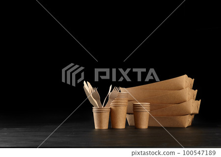 Eco friendly disposable tableware standing on dark surface against black background. Biodegradable craft dishes. Recycling concept. Close-up shot. 100547189