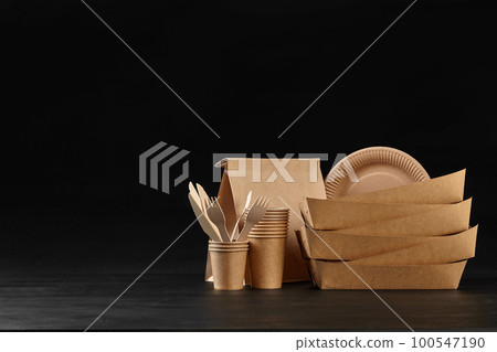 Eco friendly disposable tableware standing on dark surface against black background. Biodegradable craft dishes. Recycling concept. Close-up shot. Eco friendly disposable tableware standing on dark surface against black background. Biodegradable craft dishes. Recycling concept. Close-up shot. 100547190