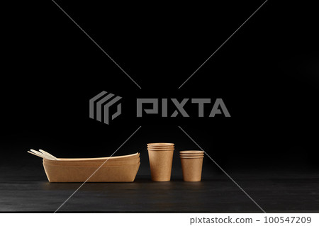 Eco friendly disposable tableware standing on dark surface against black background. Biodegradable craft dishes. Recycling concept. Close-up shot. 100547209