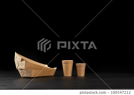 Eco friendly disposable tableware standing on dark surface against black background. Biodegradable craft dishes. Recycling concept. Close-up shot. 100547212