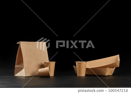 Eco friendly disposable tableware standing on dark surface against black background. Biodegradable craft dishes. Recycling concept. Close-up shot. 100547218