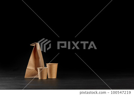 Eco friendly disposable tableware standing on dark surface against black background. Biodegradable craft dishes. Recycling concept. Close-up shot. 100547219