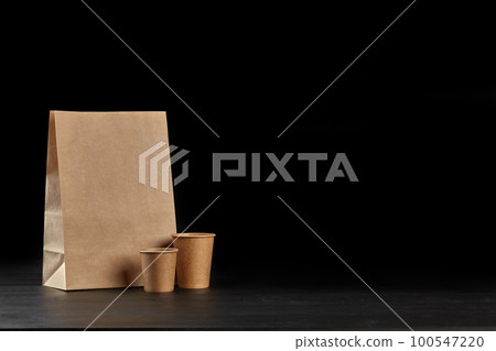 Eco friendly disposable tableware standing on dark surface against black background. Biodegradable craft dishes. Recycling concept. Close-up shot. 100547220