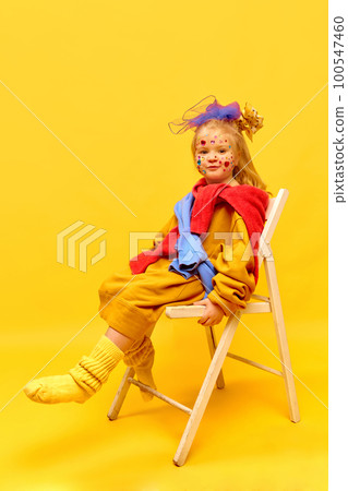 Photo of sweet little girl wearing bow, sitting on chair and dangling feet over yellow background Photo of sweet little girl wearing bow, sitting on chair and dangling feet over yellow background 100547460
