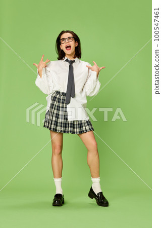 Portrait of young beautiful woman in checkered skirt and white shirt emotionally cheerfully posing against green studio background 100547461