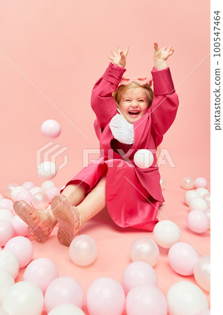 Photo of little girl with blond hair wearing pink clothes and sanglasses, playing with balls and smiling over pink background. 100547464