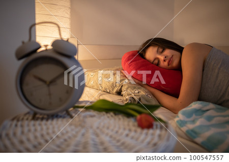 A young woman sleeps snuggled into her red pillow. 100547557