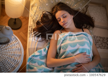 A girl with long hair sleeps peacefully on her bed. A girl with long hair sleeps peacefully on her bed. 100547629