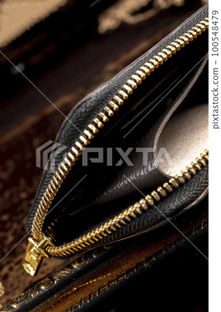 Leather wallet with a golden zipper close-up on a dark background. 100548479