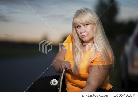 Portrait of a plump european woman in a sports tank top with a skateboard. 100549197