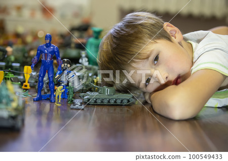 Emotional portrait of an unhappy child lying on a wooden floor with his plastic block toy, Shot of a bored child's face. Emotional portrait of an unhappy child lying on a wooden floor with his plastic block toy, Shot of a bored child's face. 100549433