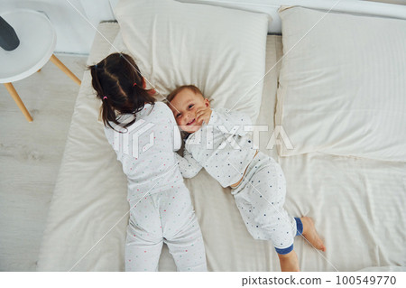 Two kids have fun while liyng down on bed. Interior and design of beautiful modern bedroom at daytime 100549770
