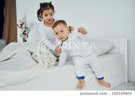 Two kids have fun while liyng down on bed. Interior and design of beautiful modern bedroom at daytime 100549803