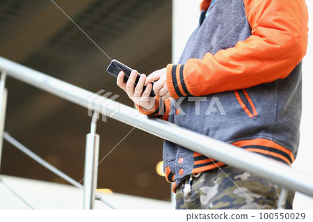 Smartphone in hand of young man standing on stairs outdoors 100550029