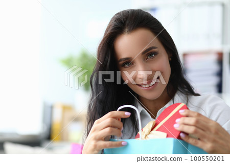 Smiling beautiful woman takes out gift from package 100550201