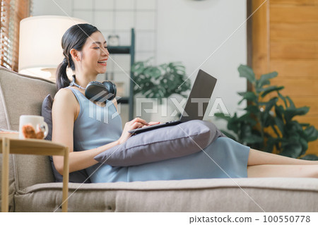 Happy young businesswoman is shown working on a laptop computer in her home office. The image represents the concept of working from home. 100550778