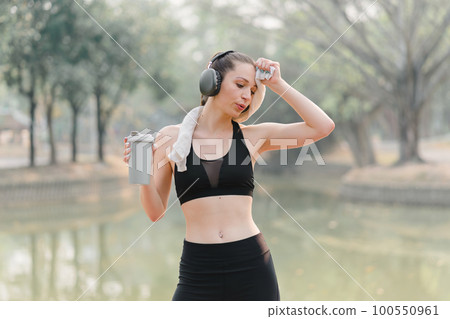 A tired woman is resting after a workout. The athlete is taking a break while contemplating her goals, progress, and performance. 100550961
