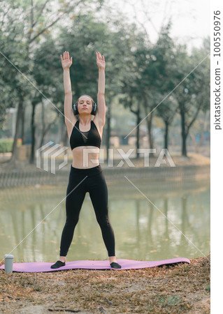 A beautiful sportswoman in sportswear is practicing yoga exercises in an Autumn city park background. 100550976
