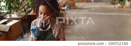 Woman florist wearing apron is taking notes during working day in floral studio 100552188