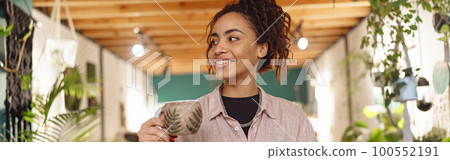 Smiling woman floristic studio owner standing with cup of tea and laptop during break 100552191