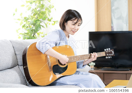 微笑的女人坐在沙發上彈吉他 微笑的女人坐在沙發上彈吉他 100554396