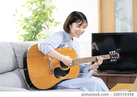 微笑的女人坐在沙發上彈吉他 100554398