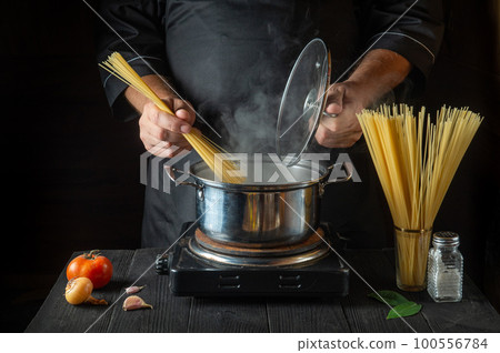 Chef prepares Italian pasta in a saucepan with vegetables. Close-up of cook hands while cooking in restaurant kitchen. Free advertising space 100556784