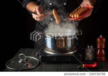 The cook cooks Vienna sausage in a saucepan. Working environment in the restaurant kitchen. Delicious breakfast or dinner The cook cooks Vienna sausage in a saucepan. Working environment in the restaurant kitchen. Delicious breakfast or dinner 100556796