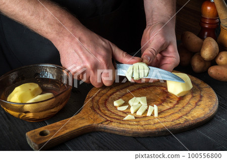 Before preparing the national dish, the chef cuts raw potatoes into small pieces with a knife. Close-up of a cook hands while working in a restaurant kitchen 100556800