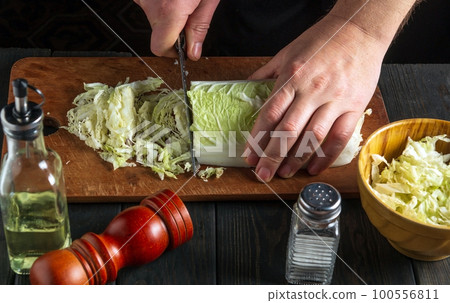 The chef prepares a salad of napa cabbage. Close-up of a chef's hand cutting cabbage with a knife on cutting board 100556811