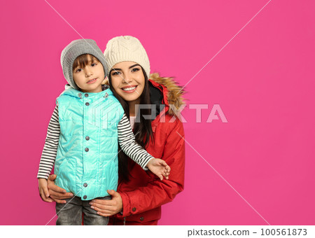 Happy mother and son in warm clothes on pink background, space for text. Winter vacation Happy mother and son in warm clothes on pink background, space for text. Winter vacation 100561873