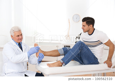 Male orthopedist checking patient's foot in clinic 100562310