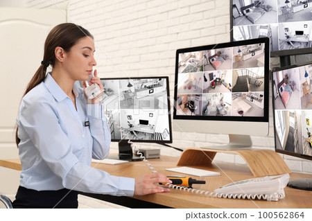 Female security guard talking by telephone near monitors at workplace Female security guard talking by telephone near monitors at workplace 100562864