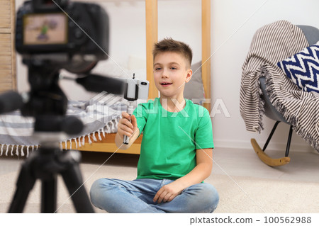 Cute little blogger with phone and selfie stick recording video at home Cute little blogger with phone and selfie stick recording video at home 100562988