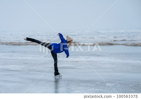 Caucasian woman in a blue sweater is skating on a frozen lake. Figure skater performs a swallow.  100563378