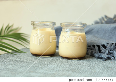 Caramel pudding in a glass jar on table  100563535