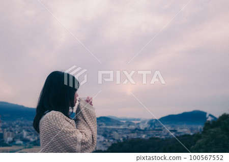 照片中一位女士拿著咖啡杯站在早晨的陽光下，背景是城市 100567552