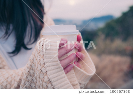 Photo of a woman holding a coffee cup standing in the morning sun with the city in the background 100567568
