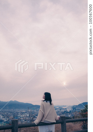 照片中一位女士拿著咖啡杯站在早晨的陽光下，背景是城市 100567600