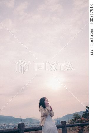 一位手持智能手機的女士站在晨曦中的照片,背景是城市 一位手持智能手機的女士站在晨曦中的照片,背景是城市 100567918