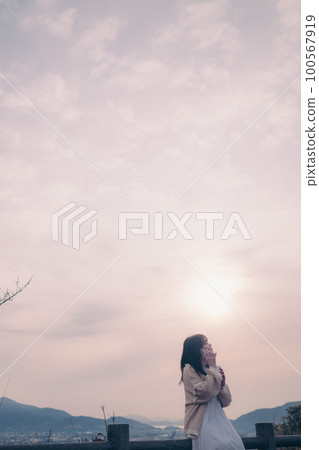 一位手持智能手機的女士站在晨曦中的照片,背景是城市 一位手持智能手機的女士站在晨曦中的照片,背景是城市 100567919