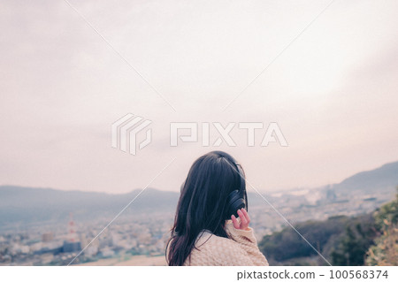 Photo of a woman listening to music with the city in the background in the morning sun Photo of a woman listening to music with the city in the background in the morning sun 100568374