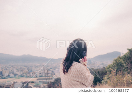 照片中一位女士在早晨的陽光下以城市為背景聽音樂 100568377