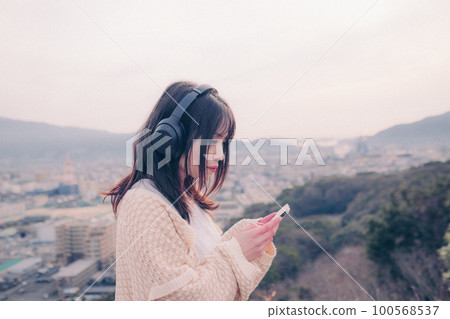 Photo of a woman listening to music with the city in the background in the morning sun Photo of a woman listening to music with the city in the background in the morning sun 100568537
