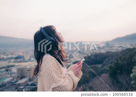 Photo of a woman listening to music with the city in the background in the morning sun Photo of a woman listening to music with the city in the background in the morning sun 100568538