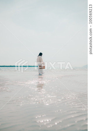 A photo of a woman holding dried flowers and a basket on the beach 100569213