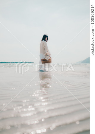 A photo of a woman holding dried flowers and a basket on the beach 100569214