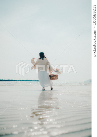 A photo of a woman holding dried flowers and a basket on the beach 100569215