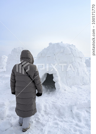 A woman near igloo, a traditional shelter of the northern peoples from the cold, made of snow bricks 100571770